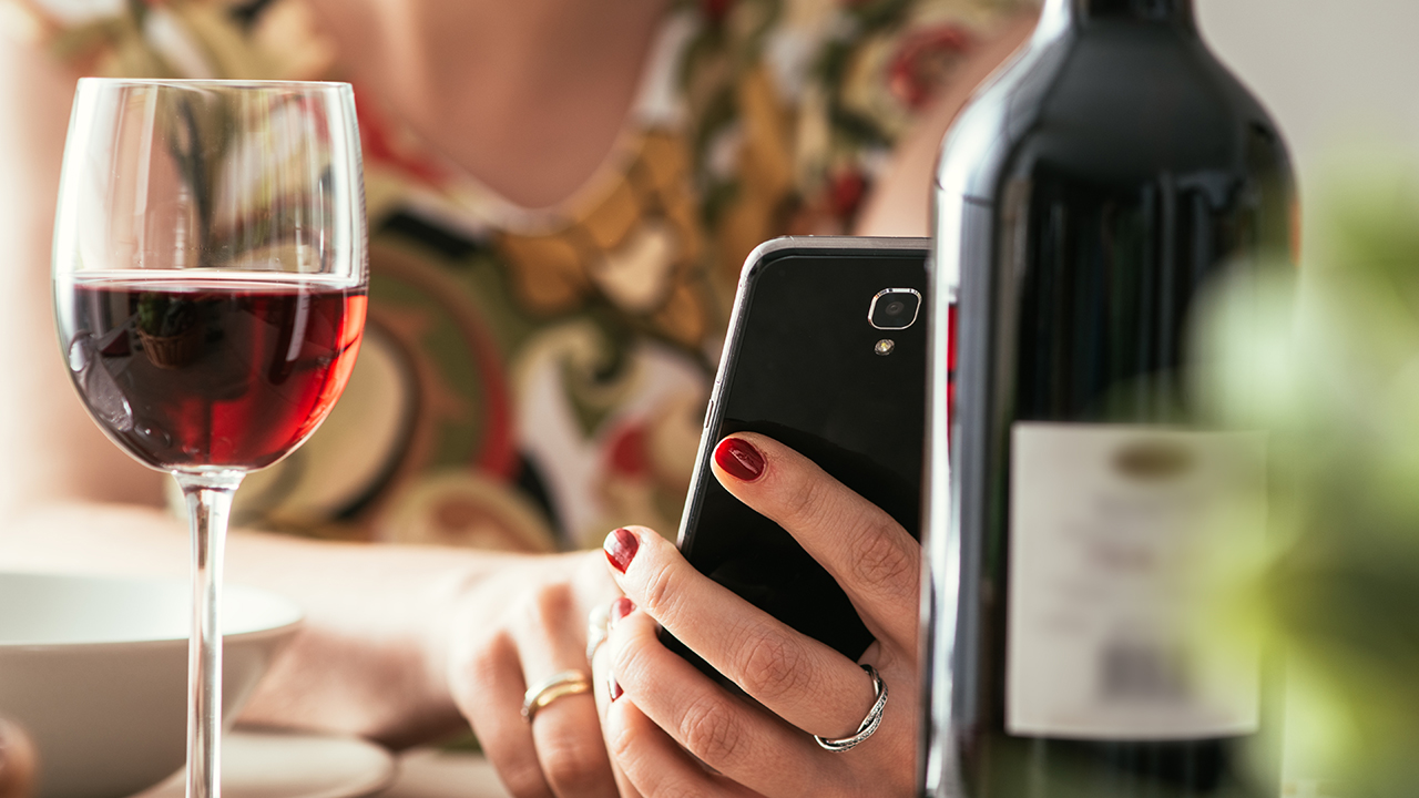 ワインを飲みながらスマートフォンを持つ女性