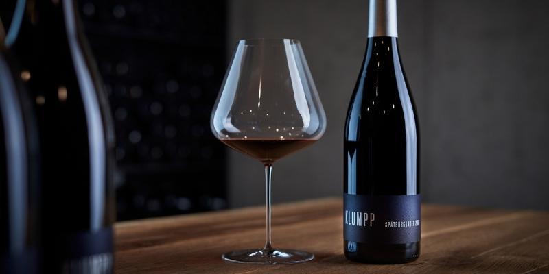 木目のテーブルに置かれたワインボトルと赤ワインの入ったブルゴーニュグラス